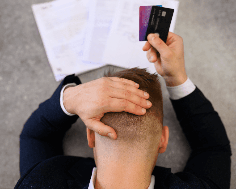 Stressed man holding his head holding multiple credit cards